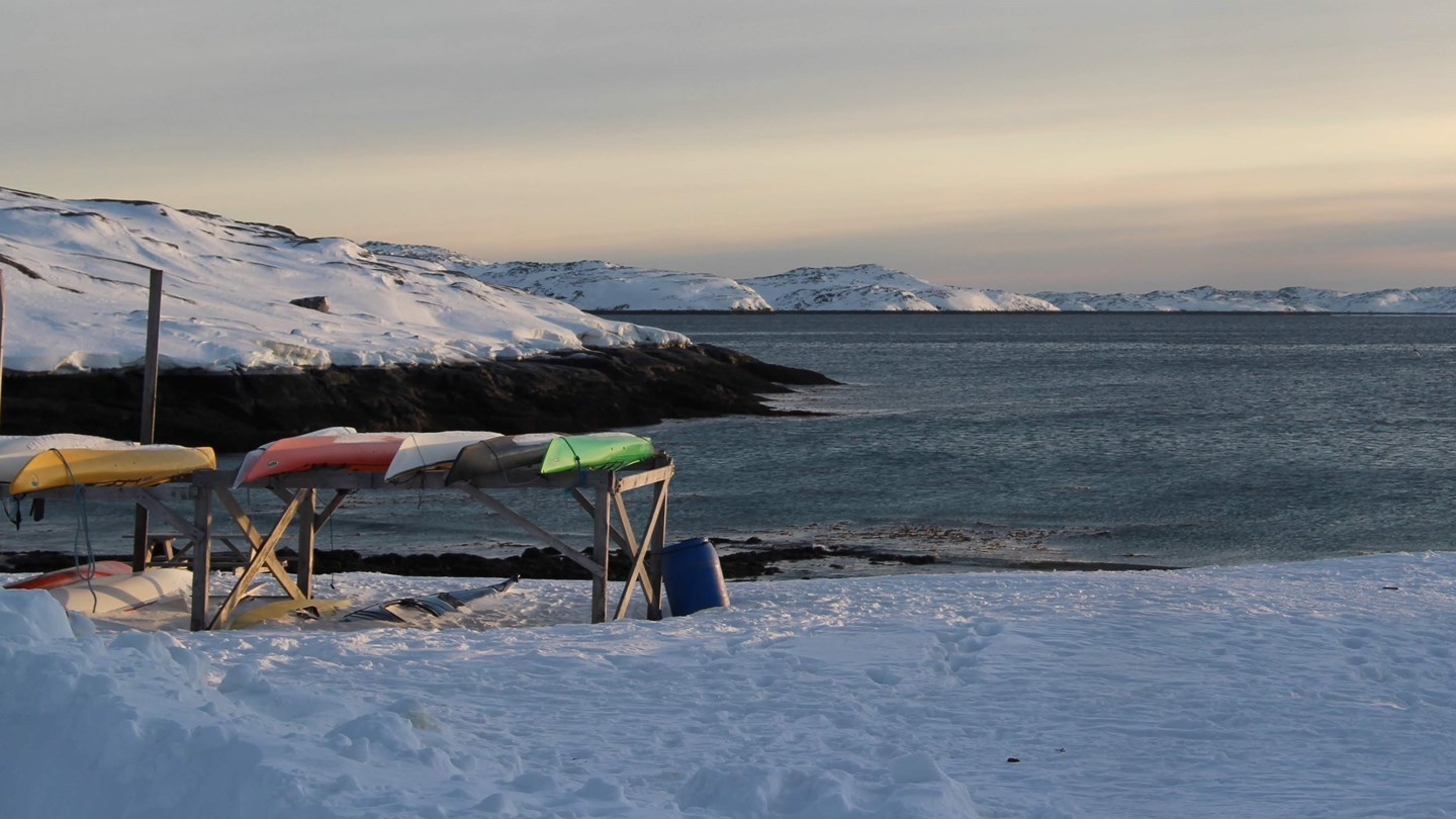 Billedet viser kajakker på bredden med fjord i baggrunden 
